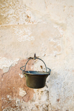 Metal pot hanging from hook in old flaking off wall