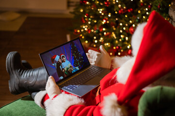 Happy mom and son talking to santa claus by video chat on a laptop. Woman and boy remotely wishes...