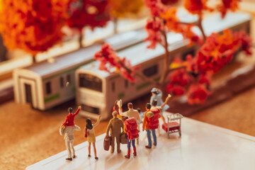 Miniature toy figurines of a group passangers waiting or waving at a train at a platform in autumn or fall season concept -  warm tone filter applied.
