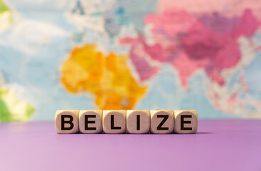 The word Belize written with wooden dices in front of a purple background and a geographic map