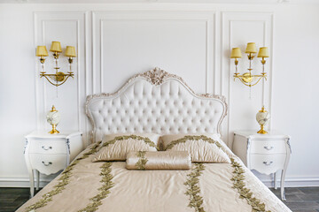 King size bed with cushioned and buttoned headboard in hotel room with classic baroque style interior. Close up, copy space, background.