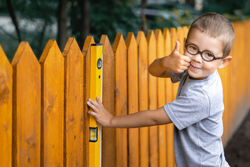 A little boy with round glasses holding a construction level and shows thump up - he plays...