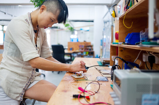 Young adult woman in workshop working on design of printed circuit board.
