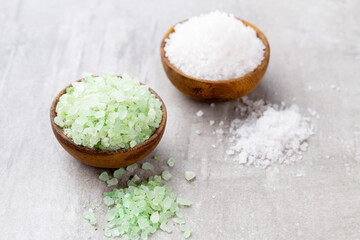 Sea salt in bowl, aroma oil in bottles, Wellness and flowers on grey textured background and flowers on vintage wooden background. Selective focus.