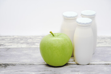Natural liquid yogurt with probiotics in small plastic bottles and yellow apple on wood table. Healthy, balanced diet food, healthy breakfast, dairy products with fruit additives. Space for text