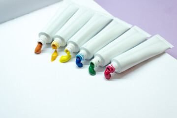 White tubes of paint on a lavender background. Multi-colored paints. Flatley.