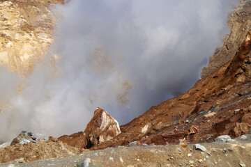 Mutnovsky volcano. Large yellow-gray stone on the edge of the fumarole field. Steaming fumaroles in the crater of the active volcano