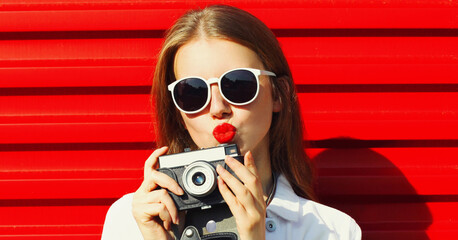 Portrait of young woman photographer with vintage film camera over red background