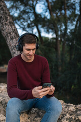 Boy listening to music with wireless headphones and using his cell phone sitting down.
