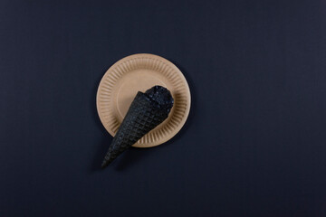 Black Friday concept. Melted black ice cream in traditional ice cream cones on the paper plate. Flat lay. Copy space.