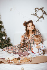 Portrait of a happy mother and a charming child at Christmas in a bright interior playing with a Christmas ball