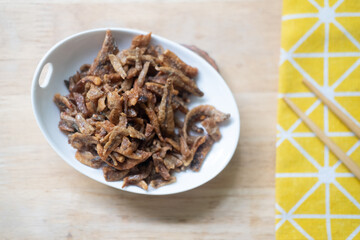 Fried crispy small fish sweet flavored put in ceramics dish with chopsticks.