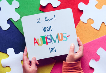 Hands hold board. Text in German means April 2 Autism World Awareness day. Puzzle, layered felt.
