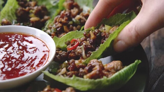 Woman take Chilli Beef Lettuce Wraps from black plate