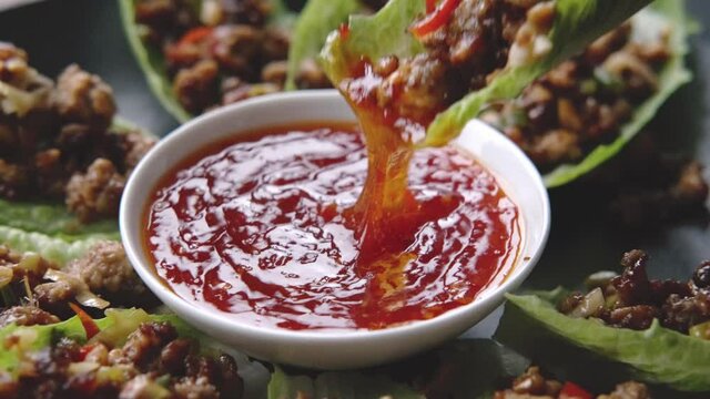 Woman dipped, dip Chilli Beef Lettuce Wraps in hot sauce