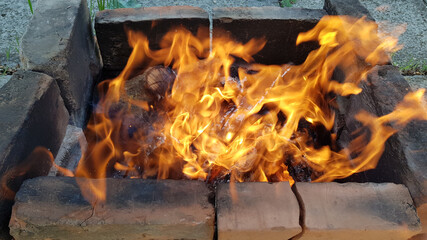 Obraz premium Mangal campfire with bright red flame in old charcoal brazier made from burnt smoky bricks on the ground