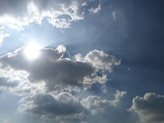 Scenic blue sky with clouds, dramatic sky with bright light from the sun behind the fluffy clouds.