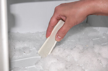 Woman cleanes the refrigerator. Woman's hand with ice scraper. Defrosting of freezer.