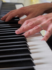 Fototapeta premium Close up point of focus on one of two hands playing a keyboard.Wedding ring on finger.Musician.Vertical Image