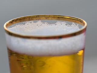  Close view of the froth in a newly poured gold rimmed glass of beer.Focus on back of glass deliberate blur to foreground.Drink