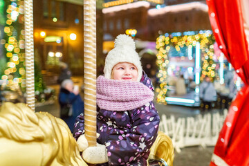 Fototapeta na wymiar A little girl in warm clothes rides on a Christmas carousel with lights. Christmas market, night time