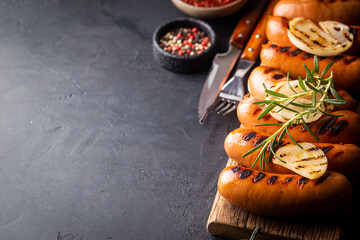Fried delicious sausages with tomato sauce and herbs on cutting board, black background.