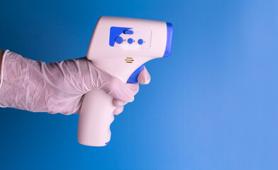 Contactless thermometer in the hand of a man in a medical glove on a light blue background. Copy space.