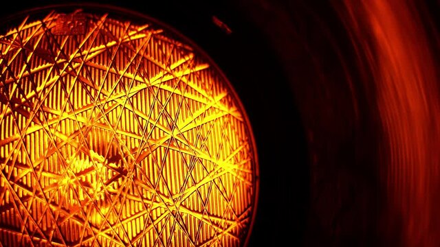 Handheld suggestive close-up shot of an alert yellow flashing light of a traffic light or semaphore at night. Balck background.