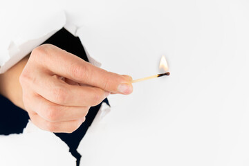 The girl's hand holds a burning match through a hole in the wall of the wall.