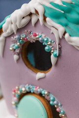 A beautiful colored gingerbread house decorated with glaze with caramel windows on a dark background with powdered sugar snow. New year gift