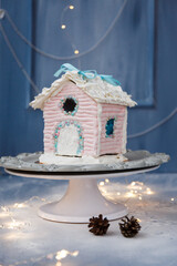 A beautiful colored gingerbread house decorated with glaze with caramel windows on a dark background with powdered sugar snow. New year gift