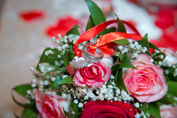 Rings on the wedding bouquet . The engagement rings are tied with ribbon Selective focus and blurred background . Gold wedding rings on a bouquet of red and white flowers.
