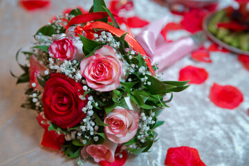 Rings on the wedding bouquet . The engagement rings are tied with ribbon Selective focus and blurred background . Gold wedding rings on a bouquet of red and white flowers.