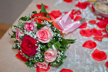 Rings on the wedding bouquet . The engagement rings are tied with ribbon Selective focus and blurred background . Gold wedding rings on a bouquet of red and white flowers.