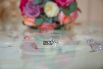 Glass table . Wedding rings next to a red flower bouquet selective focuse . Bride and groom with Engagement gold rings put on the table, and next to them lies a wedding bouquet .