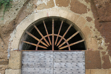 arch with a metal grate above a wooden door in a stone wall