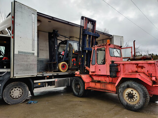 Old big diesel forklift unloading a smaller forklift