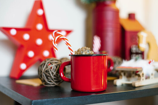 Red metal mug with cocoa and candy cane with Christmas decor