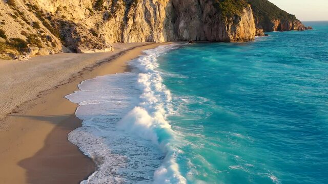 Aerial view of Milos beach at the island of Lefkada, Greece, during sunset time with golden sunlight and waves breaking the turquoise sea on the shore