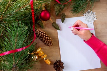 Young woman writes a New Year's greeting card or Christmas wish sheet on a white piece of paper.