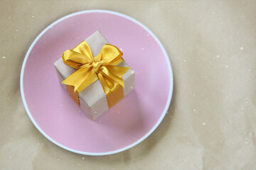 Gift box wrapped by kraft brown paper with beautiful yellow satin ribbon on pink plate background....