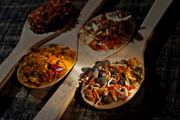 A mixture of various spices in a wooden spoon. Spices and seasonings on an old shabby board. Mix on a pile close up. Contrasting dramatic light as an artistic effect.