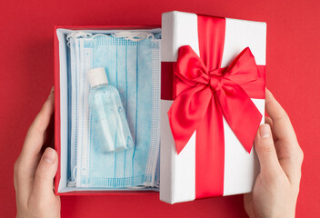 Present on Valentines day from lover concept. Top above overhead close up view photo of woman hands holding present box cap looking inside the package finding masks and antibacterial gel for hands
