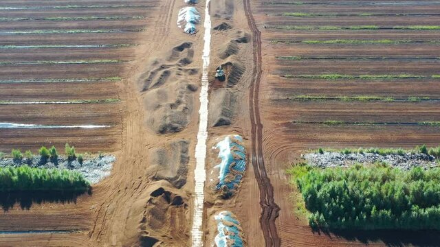 Aerial shot flying along road over peat harvesting field. Peat extraction. Piles of peat.