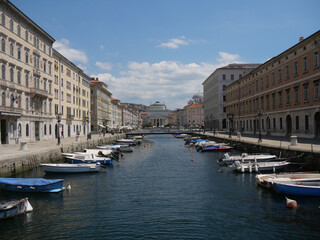 Naklejka na ściany i meble Panorama of Borgo Teresiano in Trieste, characterized by the Grand Canal, ancient buildings on both sides, and by the Church of San Paolo with neoclassical style positioned in front.