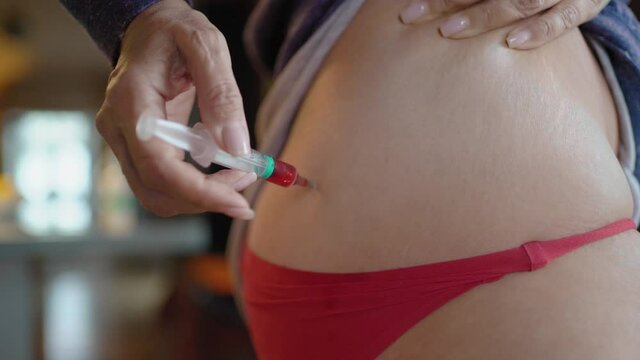 A mature woman gives herself an injection with Vitamin B, a woman sits at home with Covid-19 and gives herself a close-up syringe injections.The woman makes an injection into the intramuscularly.