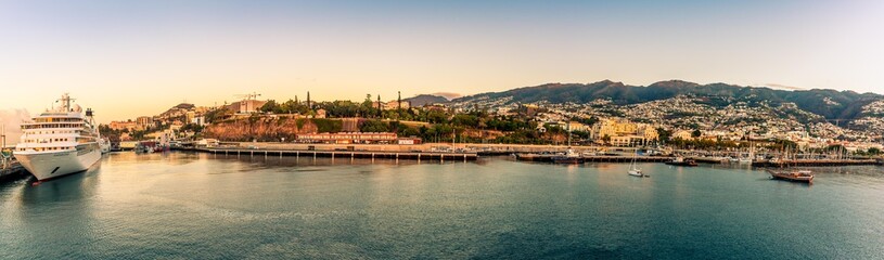 A panorama view sailing into the port of Funchal, Madeira with the shore bathed in the glow of the...