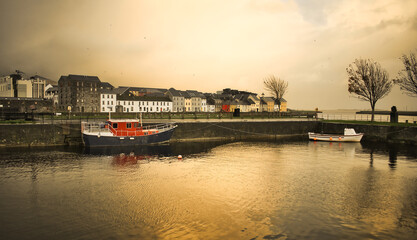 Naklejka premium Boats and houses at cloudy golden hour at Claddagh in Galway city, Ireland