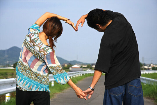 Rear View Of Couple Making Heart Shape While Standing On Road