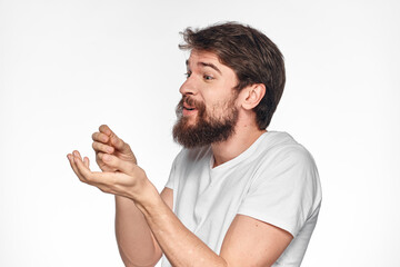 cheerful bearded man in a white t-shirt emotions gestures with his hands light background studio